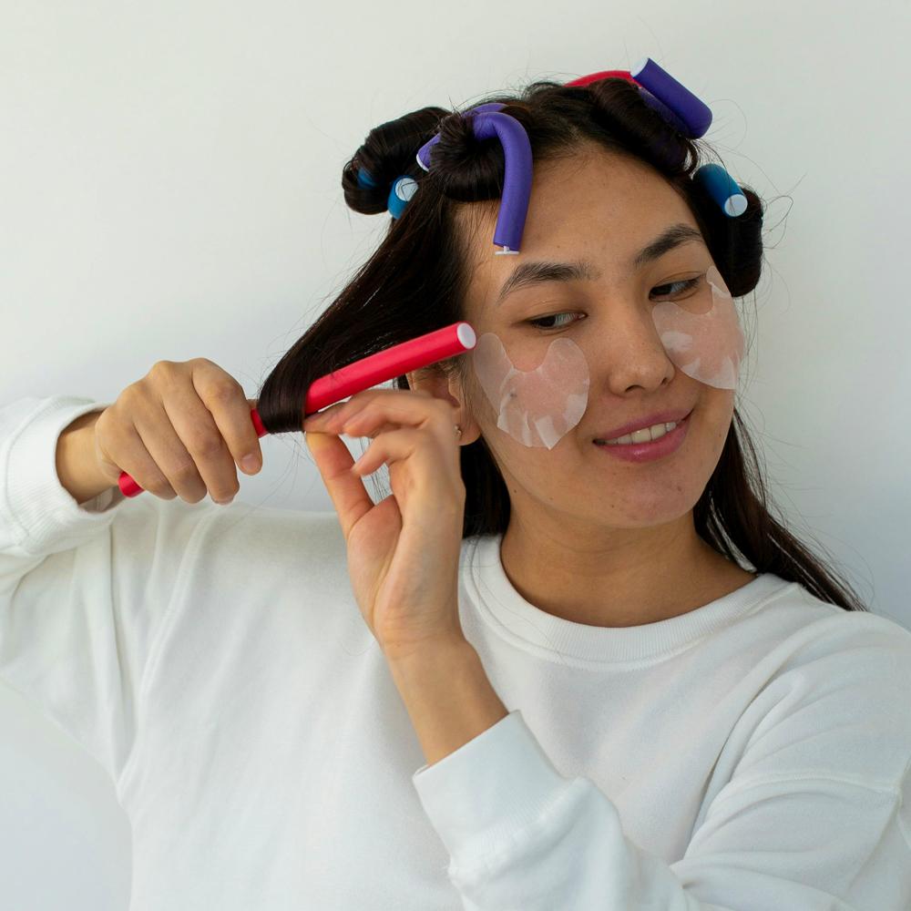 Žena si d&aacute;v&aacute; nat&aacute;čky na vlasy při dom&aacute;c&iacute;m stylingu vlasů